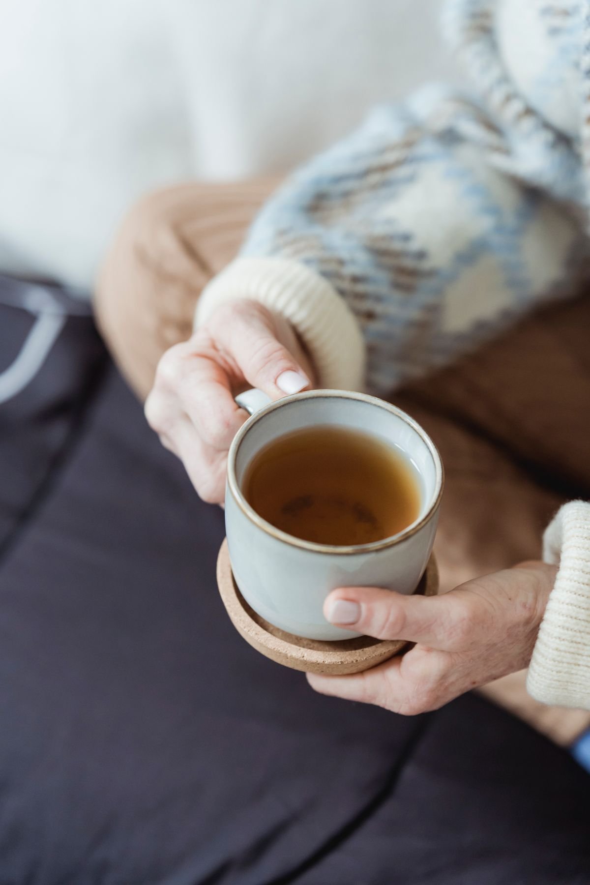 Mulher relaxando no sofá tomando chá, ambiente aconchegante com luz suave
