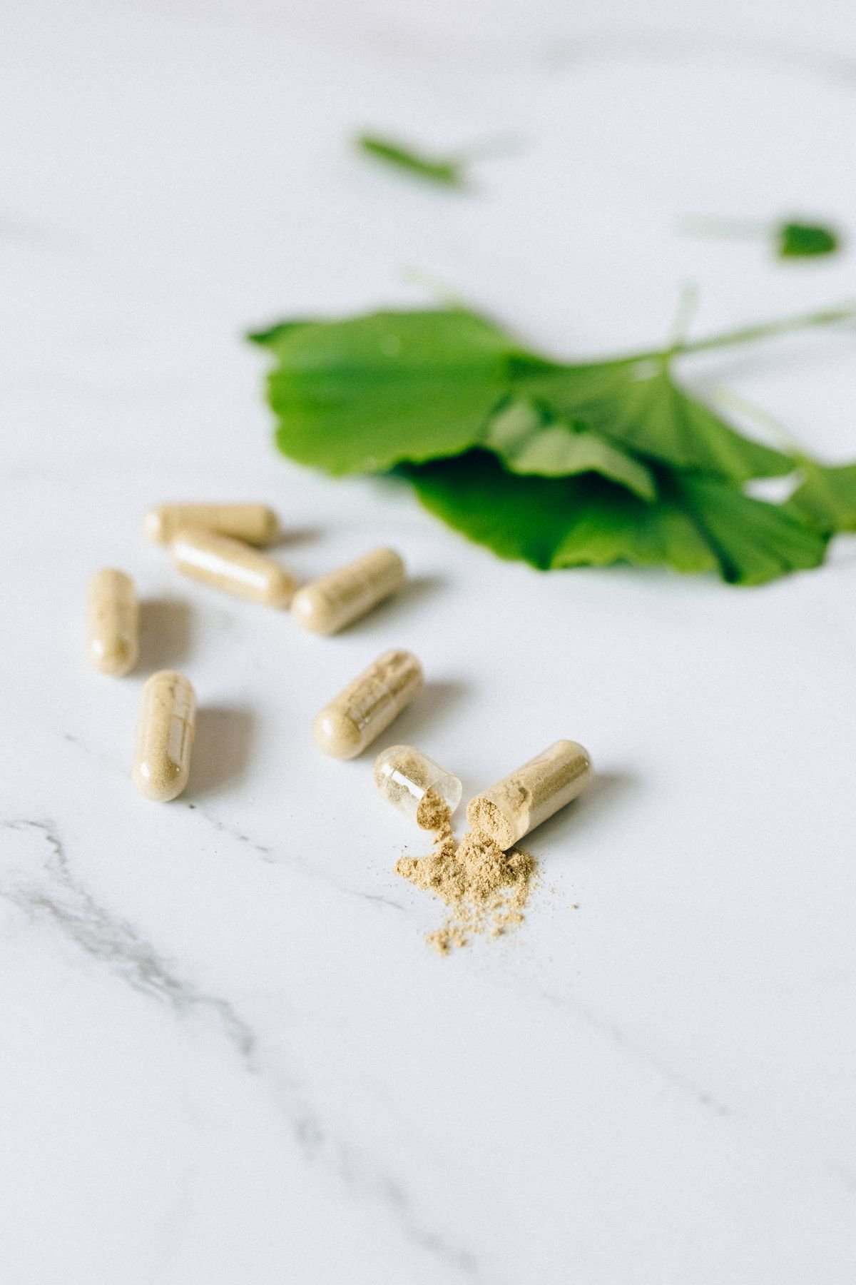 Cápsulas de suplemento herbal com folha sobre superfície de mármore
