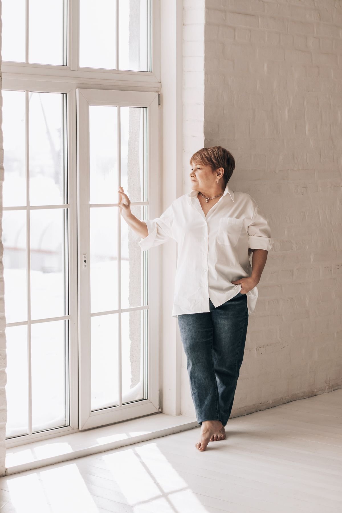 Mulher de meia-idade olhando pela janela em um momento tranquilo, luz natural