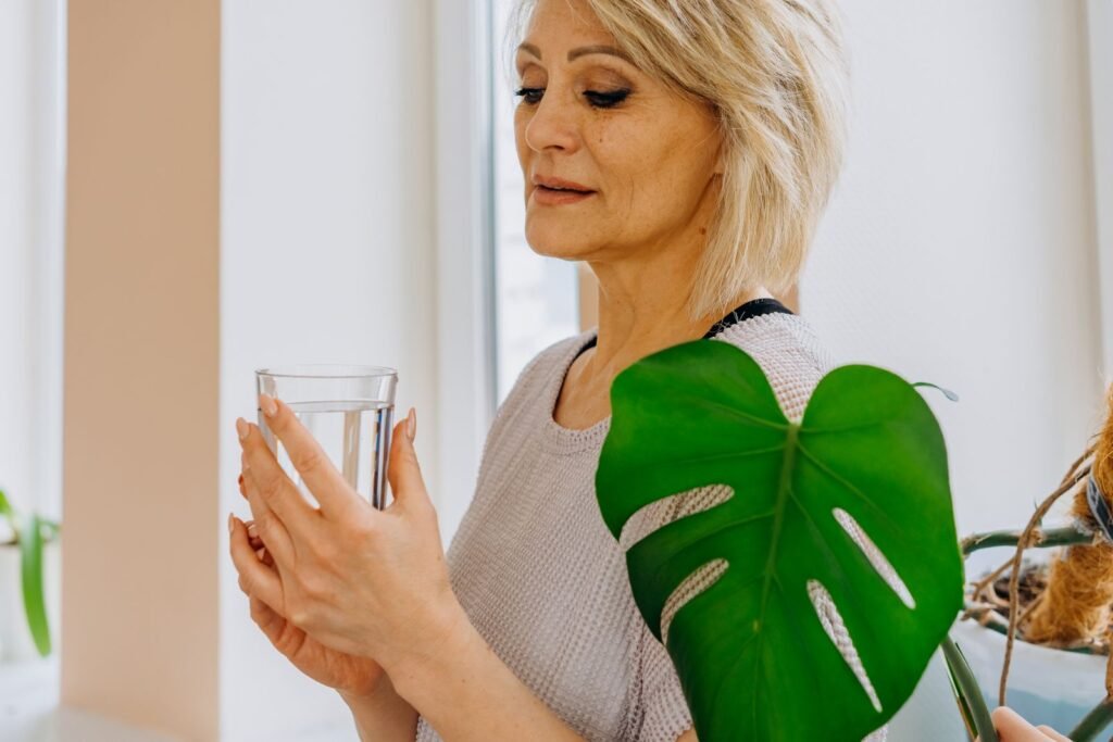 Mulher madura segurando um copo de agua perto da janela