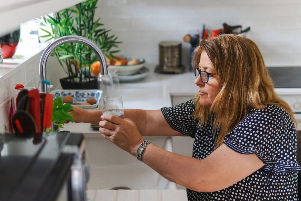 Mulher madura enchendo um copo de agua na pia da cozinha